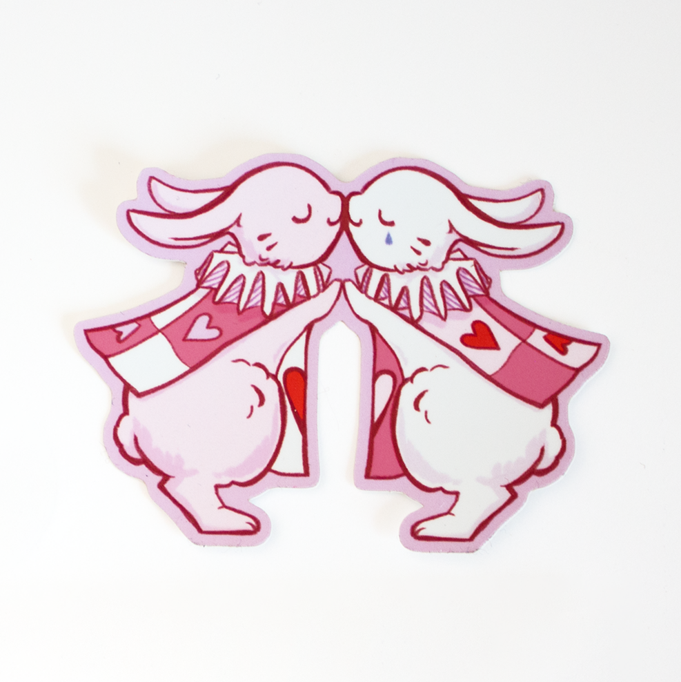 Sticker design with red foil hearts. One white rabbit and one pink rabbit kissing, both wearing harlequin outfits and jester collars like pawns of the Queen of Hearts