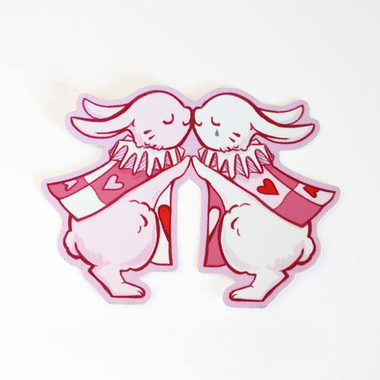 Sticker design with red foil hearts. One white rabbit and one pink rabbit kissing, both wearing harlequin outfits and jester collars like pawns of the Queen of Hearts